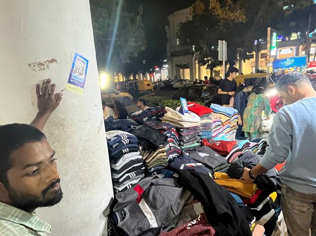 A QR code for UPI payment stuck on a column in Indian capital New Delhi’s centrepiece shopping arcade Connaught Place helps the pavement garment seller conduct brisk cash-free business. Photo by Sujoy Dhar.